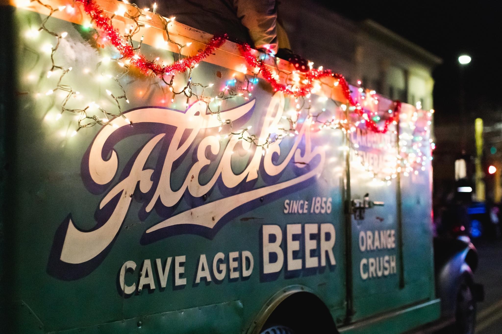 Close-up of a vintage Fleck's Cave Aged Beer and Orange Crush delivery truck decorated with festive Christmas lights and tinsel for the parade.