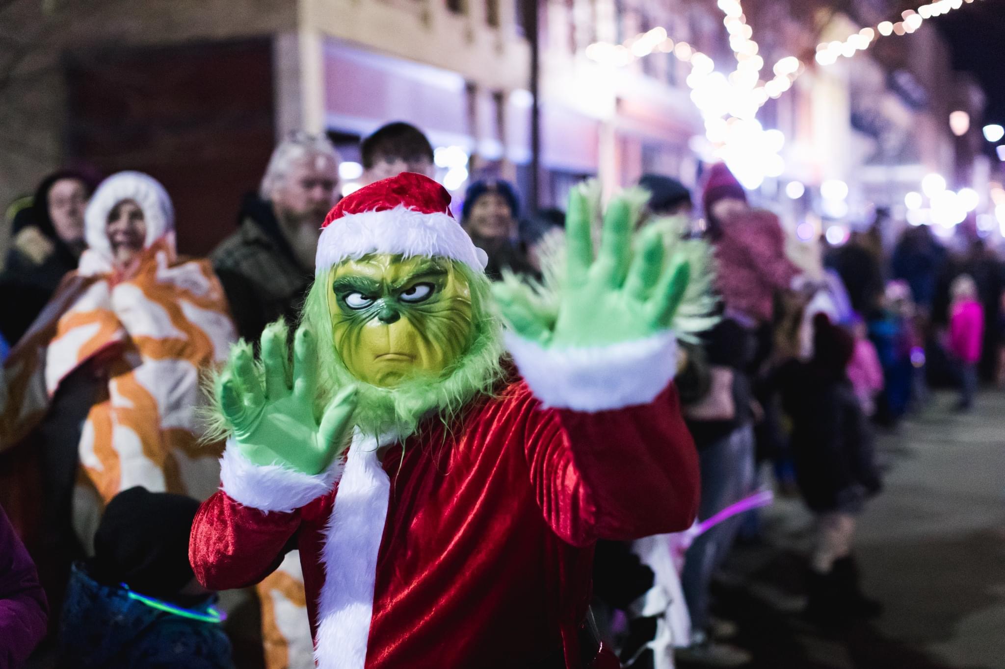 Close-up of the Grinch in a red Santa suit with furry green hands waving to the crowd during the parade of lights.